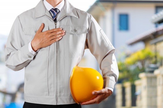 ヘルメットを持つ作業着姿の作業員