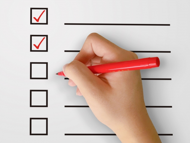 チェックリストに赤ペンでチェックを入れている手元のイメージ