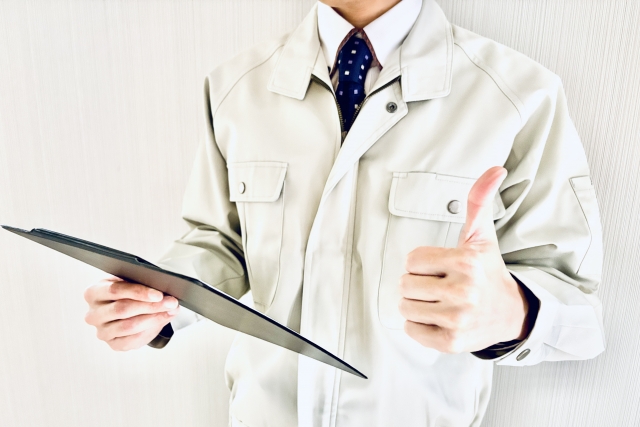 作業服を着た人物が資料を持ちサムズアップしている確認・評価のイメージ